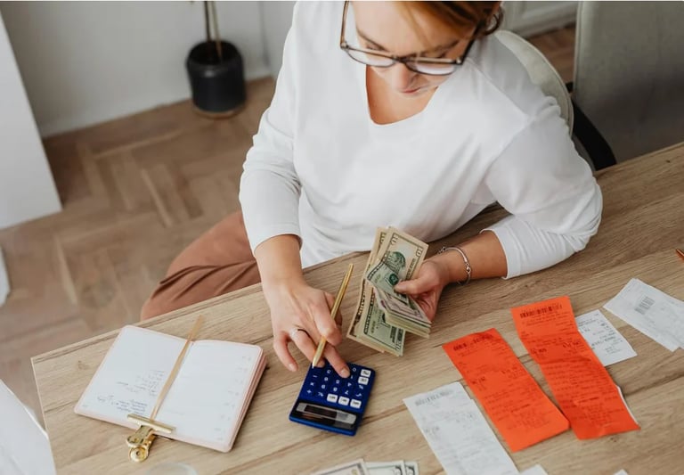 Woman counting cash at wooden desk with calculator and financial documents spread out